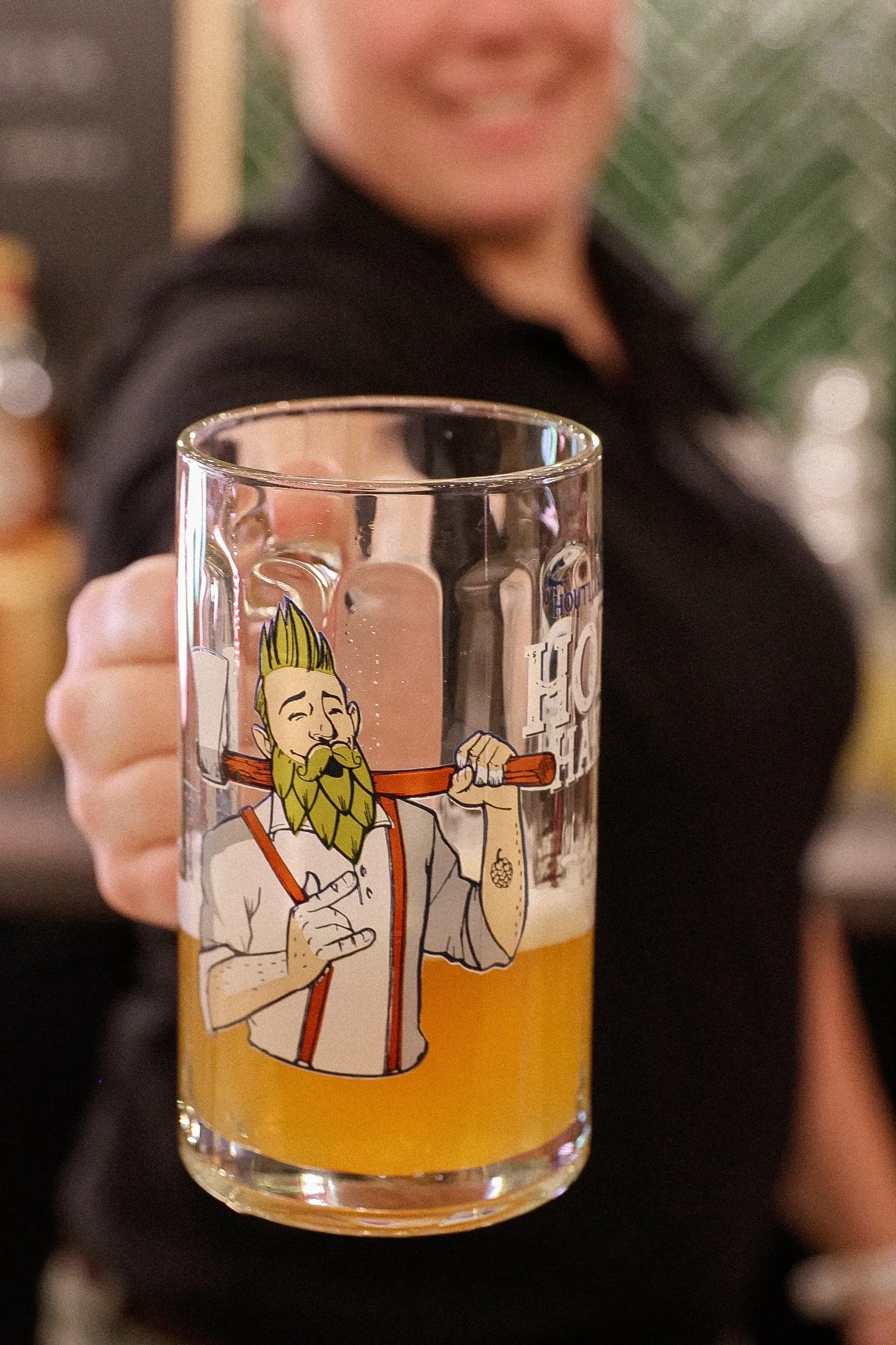 Choppe de bière levée à la main, ambiance conviviale du Hache Bar.